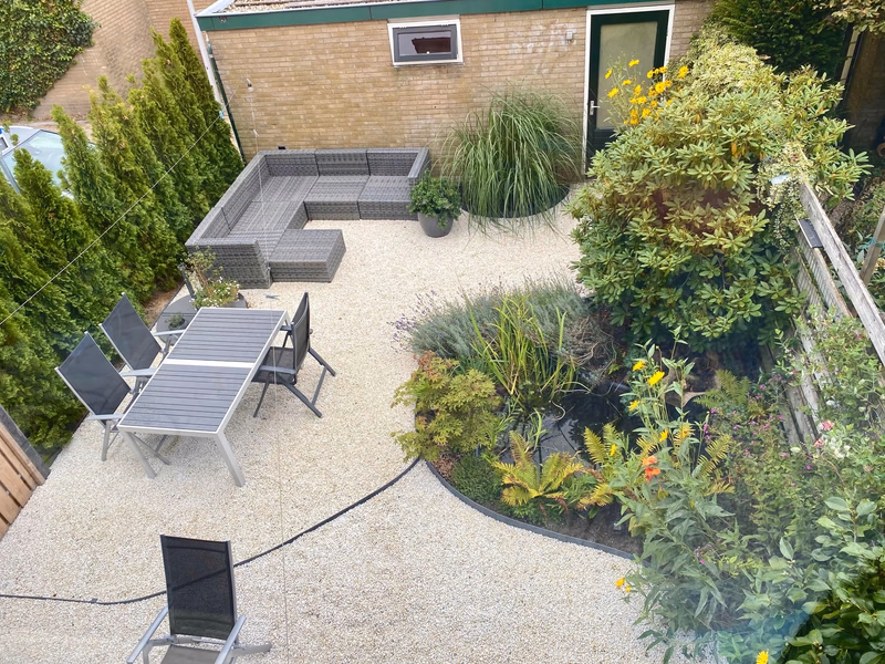 Een tuin met een terras, zithoek, groene borders en witte kwartssplit